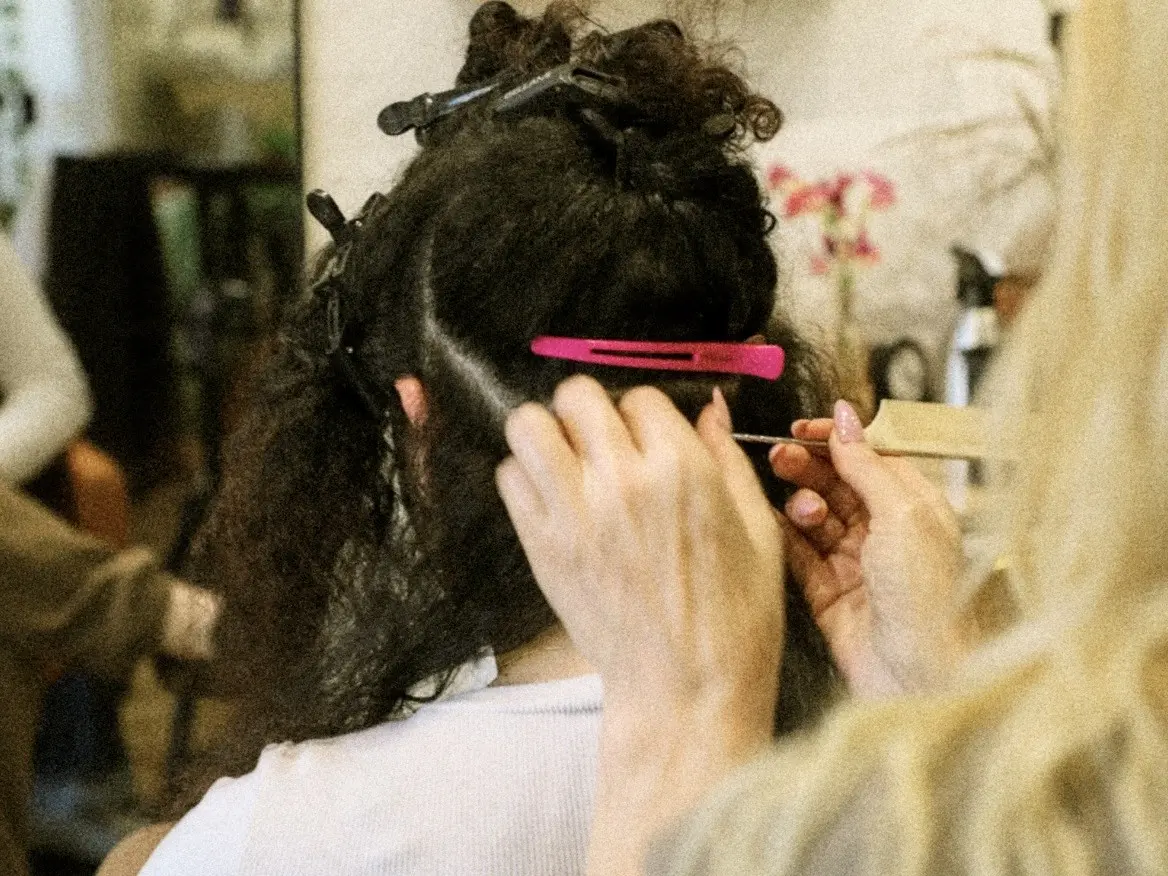 Stylist sectioning curly hair with clips in a salon. Hands gently part hair using a comb. Warm, professional atmosphere with soft focus background.